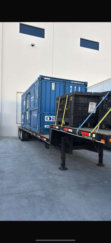 Customer flatbed loaded with a shipping container and secured crates, pulled power only